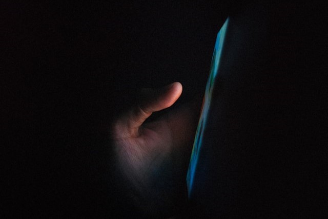暗闇の中でスマートフォンの画面を見る手元（就寝前のスマホ操作が睡眠の質に与える悪影響のイメージ）